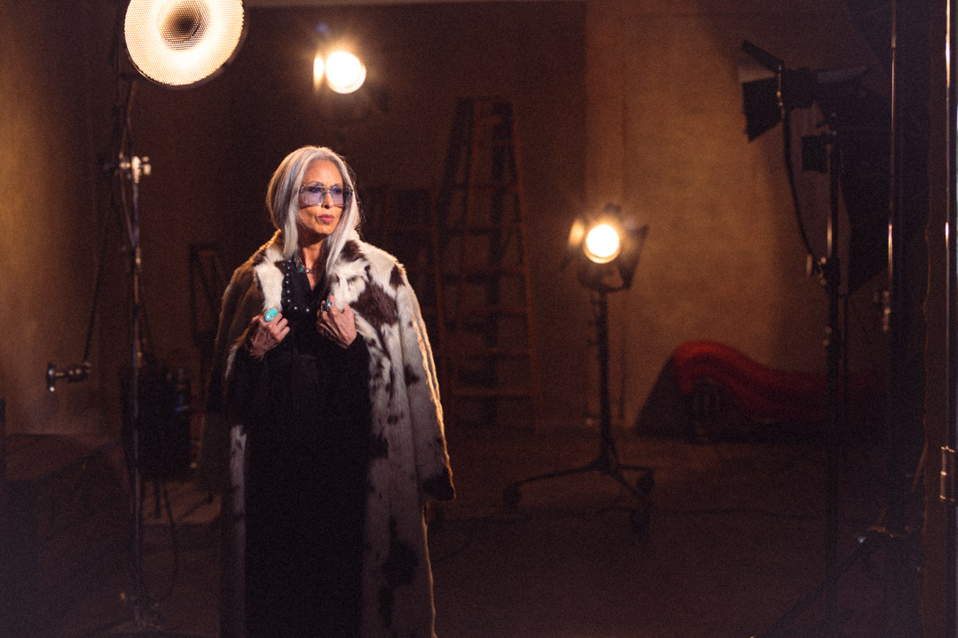 Studio portrait of a silver-haired woman in a patterned coat under warm lights